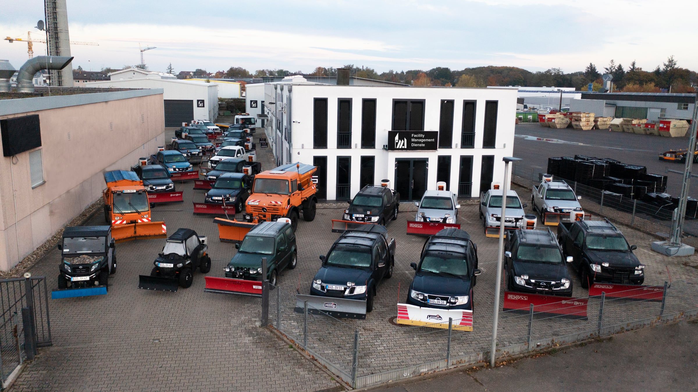 Firmengebäude der FMD mit Logo, davor der Fuhrpark für den Winterdienst: Geländewagen und Räumfahrzeuge mit Schneeschilden und Kehrbürsten