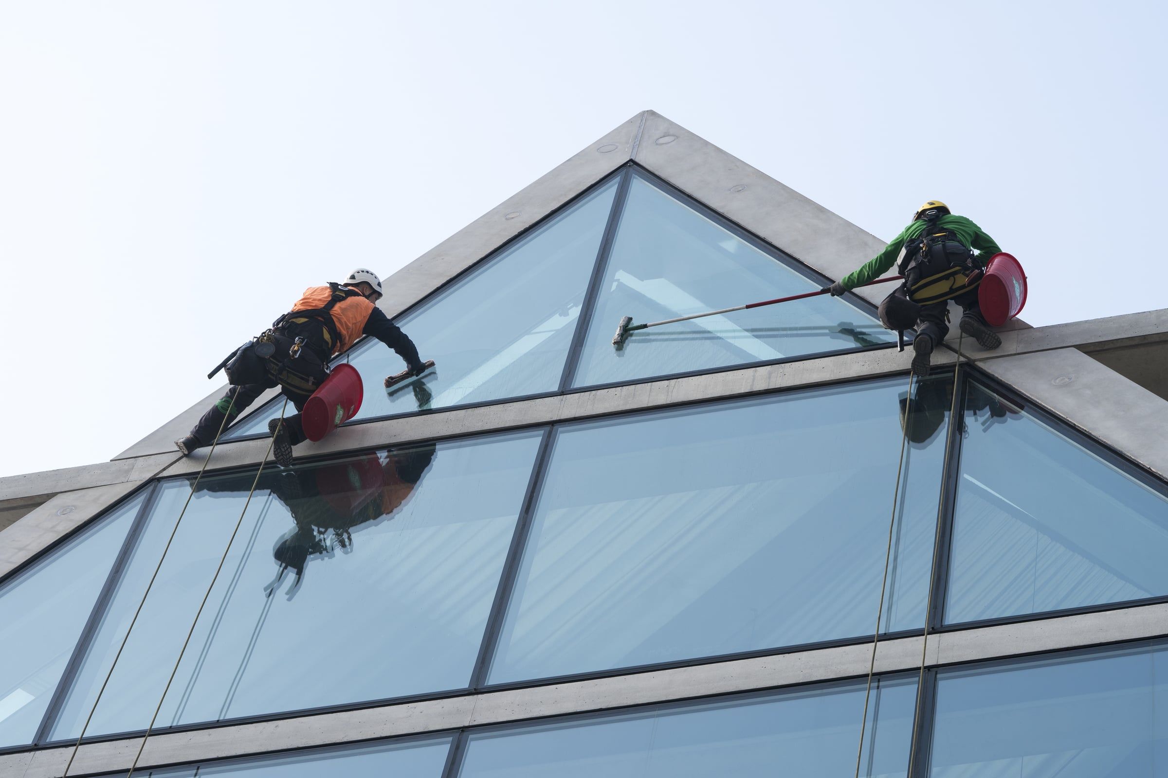 Zwei gesicherte Fensterputzer reinigen ein pyramidenförmiges Glasdach