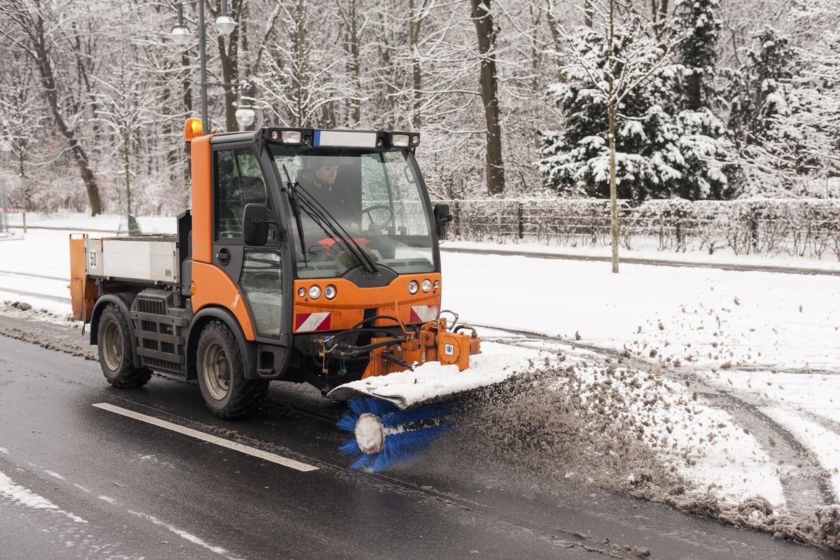 Kommunalfahrzeug mit Kehrbürste räumt Schnee von einer Straße