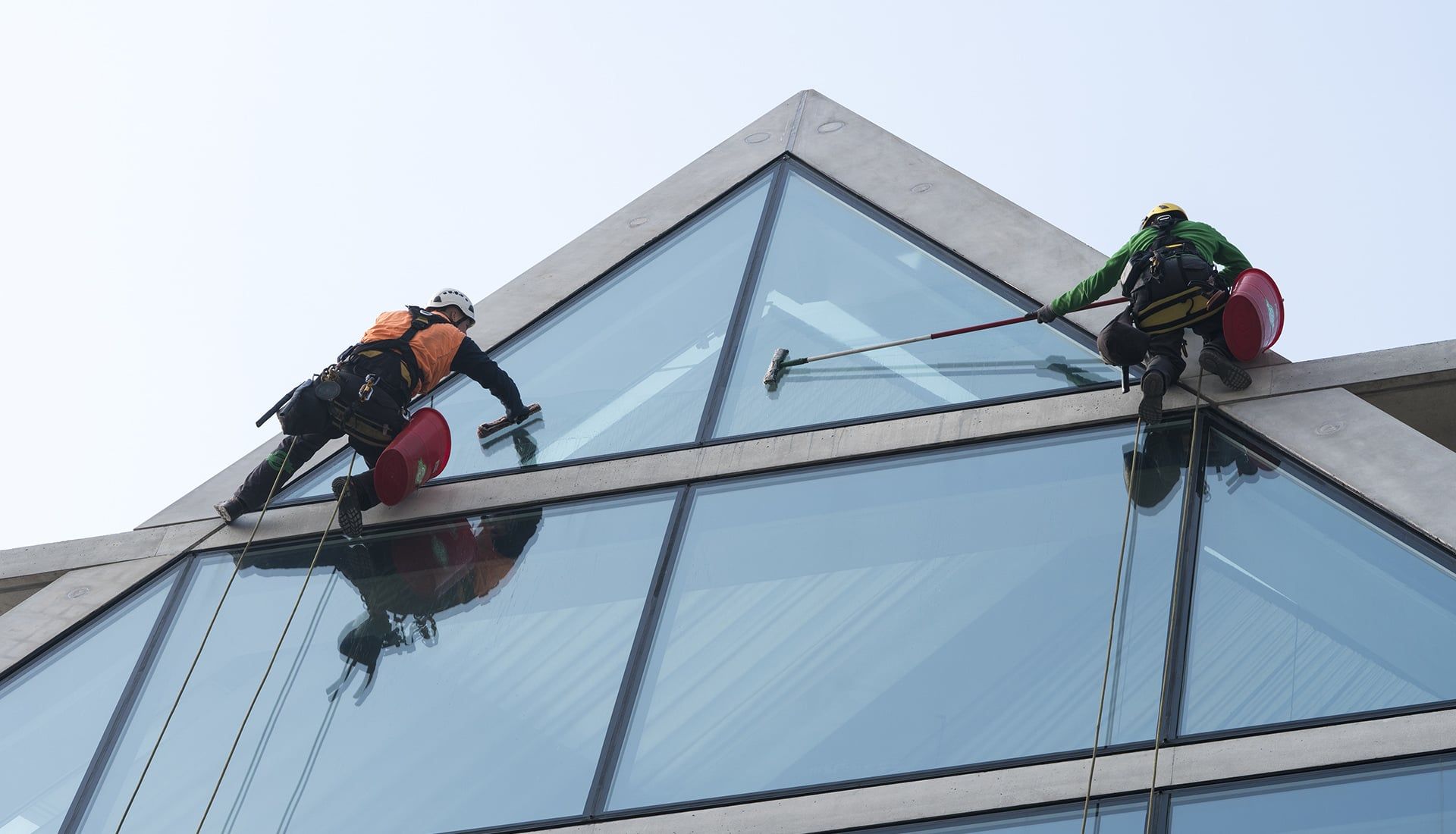 Zwei gesicherte Fensterputzer reinigen ein pyramidenförmiges Glasdach
