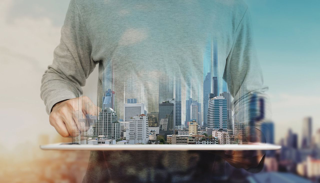 Hand über einem Tablet, aus dem die Hochhäuser einer Stadt wachsen