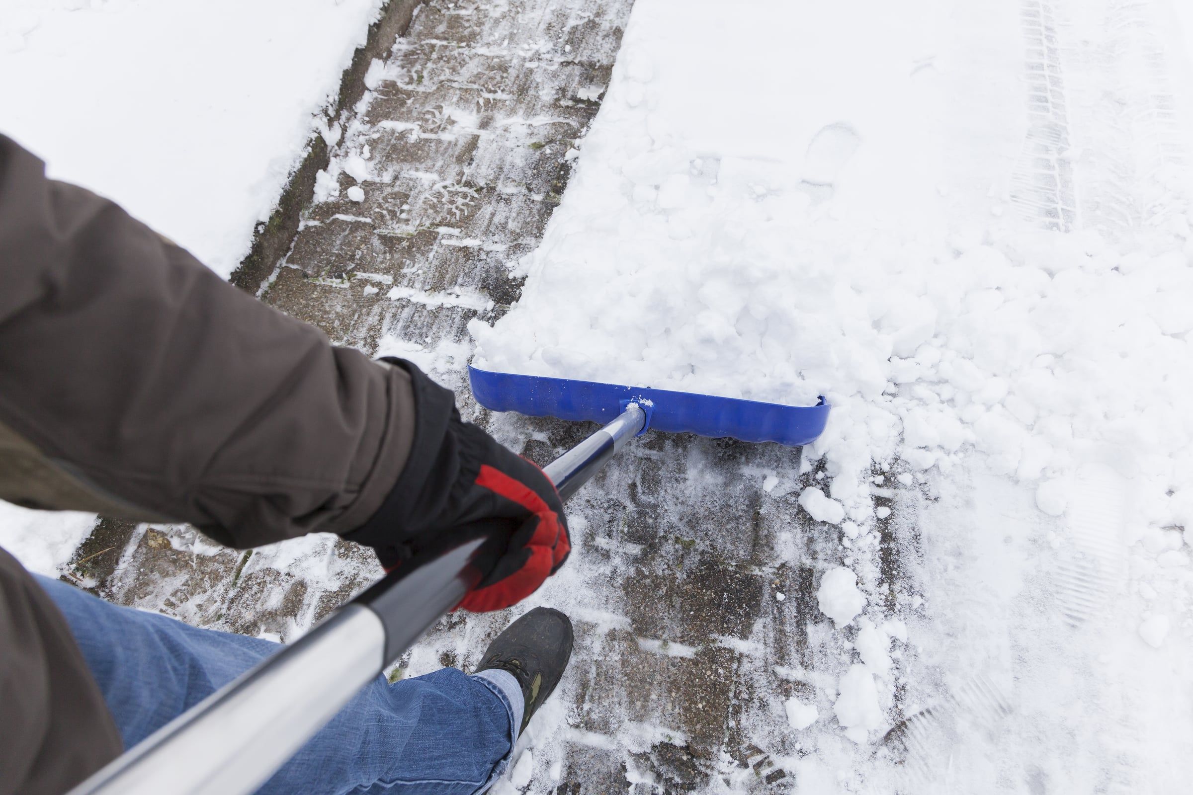 Schneeschieber räumt einen verschneiten Gehweg