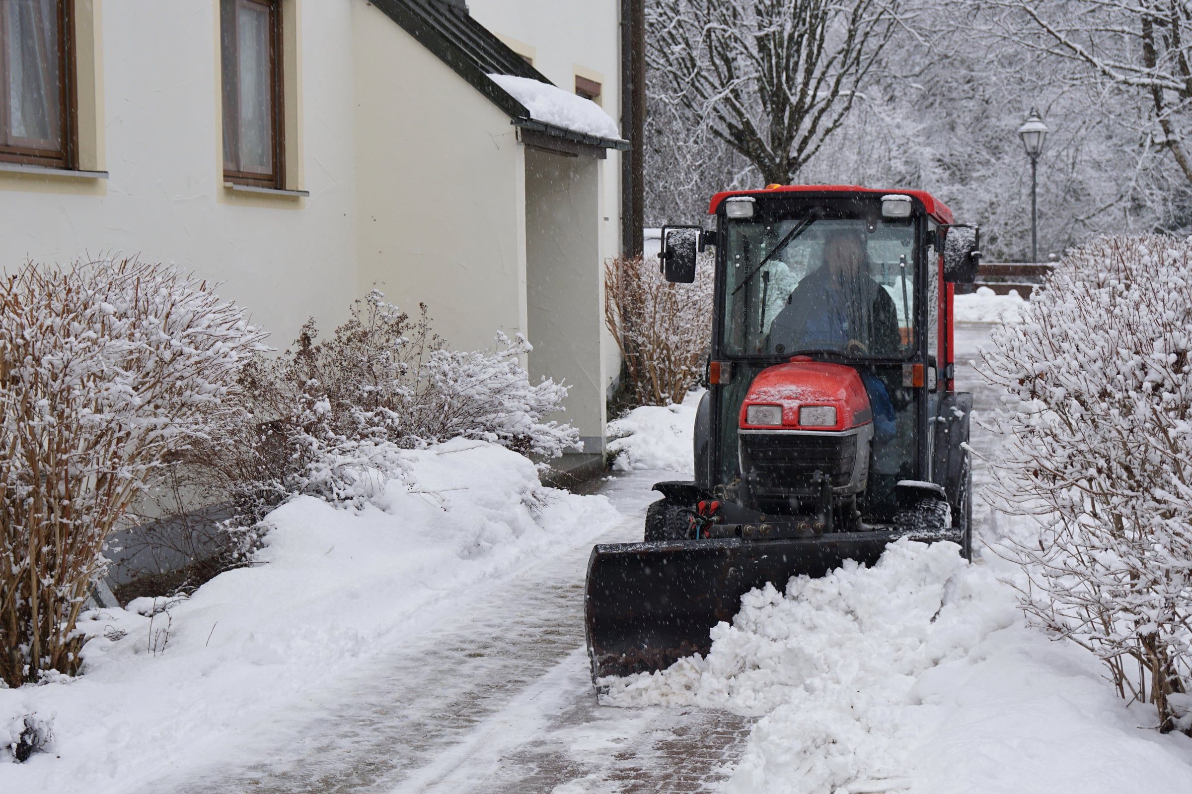 Traktor mit Räumschild räumt einen verschneiten Weg vor Wohnhäusern
